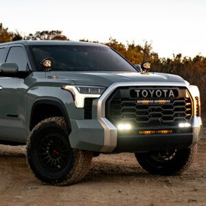 Toyota Tundra equipped with Baja Designs LED light kits, including grille-mounted light bars and pillar-mounted auxiliary lights, parked on an off-road trail at sunset.