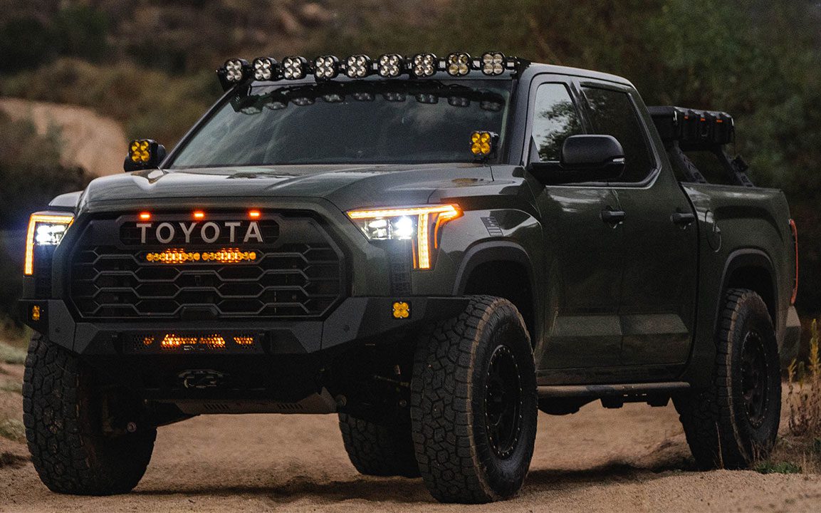 Black truck on a dirt trail with lights on.
